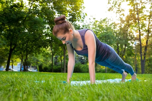 Young fitness woman meditation in a city park.Yoga at sunset in the park. Girl is practicing yoga. Fitness training outdoors. Attractive fitness woman. Workout outdoors. Healthy lifestyle