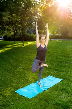 Young fitness woman meditation in a city park.Yoga at sunset in the park. Girl is practicing yoga. Fitness training outdoors. Attractive fitness woman. Workout outdoors. Healthy lifestyle. sun flare