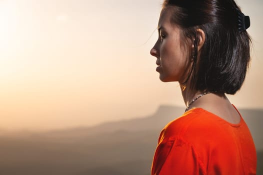 Backlit profile of a woman breathing deep fresh mountain air at morning sunrise or sunset. Calm happy woman with closed eyes.