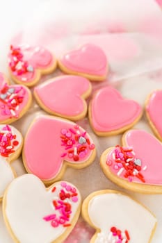 Storing heart-shaped sugar cookies with pink and white royal icing in a large plastic container.