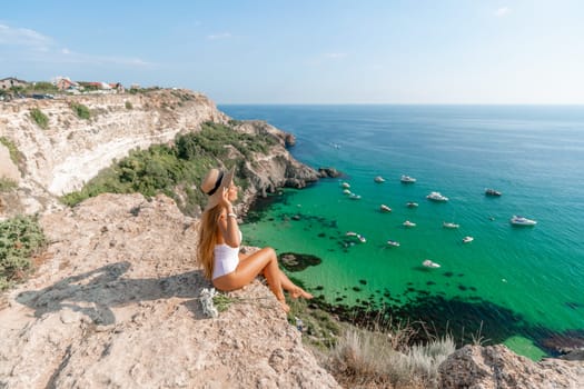 Woman travel sea. Happy woman in a beautiful location poses on a cliff high above the sea, with emerald waters and yachts in the background, while sharing her travel experiences.