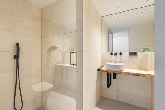 Light beige tiled bathroom with modern fixtures, sink, shower and toilet in a new building apartment. The concept of buying a home and interior design.