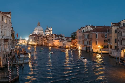 Top view of boats sailing down the Grand Canal in Venice in shining lights on the backdrop of calm water on a summer evening. The concept of wedding tourist trips in the ancient city of Italy.