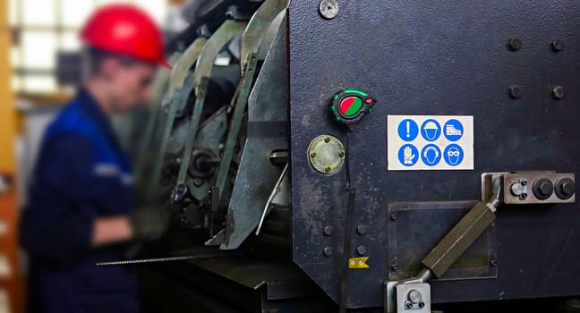 worker adjusts a punching machine at a factory. warning signs on the punching machine