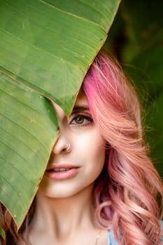 Woman portrait pink hair banana leaf. A beautiful young woman among the huge green leaves of a banana tree