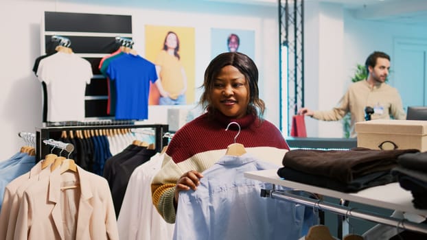 Store customer taking shirt off of hangers to buy clothes, looking at fashion boutique merchandise. Young woman shopping for new trendy collection, examining pants in clothing store.