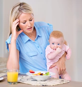 Motherhood blues. Young mother holding her baby at breakfast time looking tired