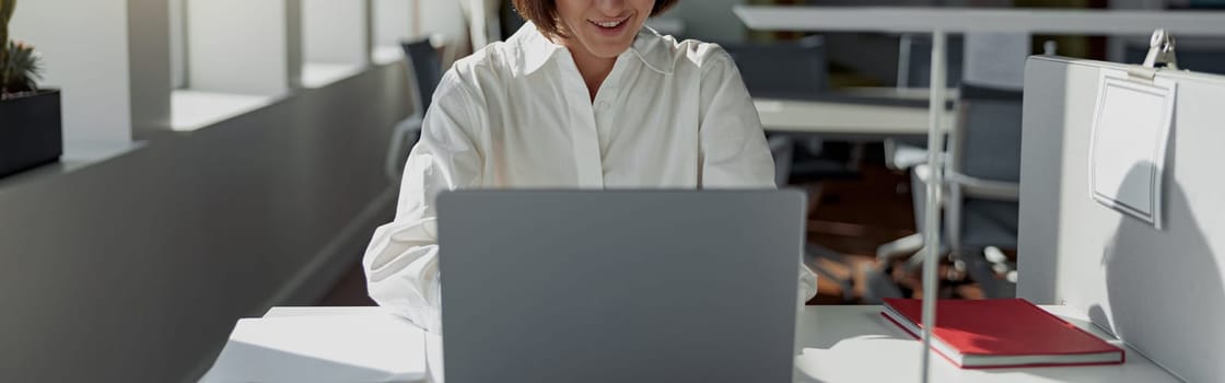 Smiling european business woman working laptop while sitting in cozy cafe. Blurred background
