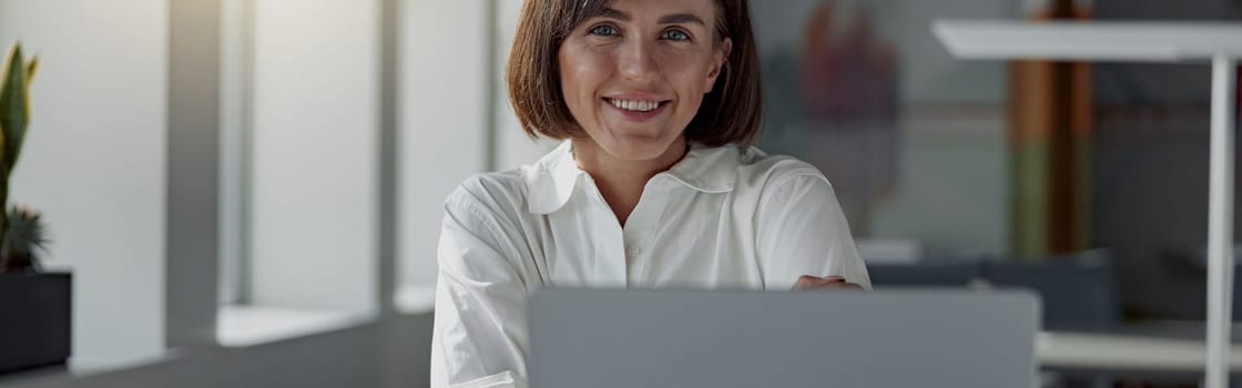 Smiling european business woman working laptop while sitting in cozy cafe. Blurred background