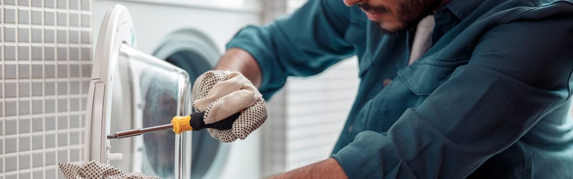 Repairman in worker suit with professional equipment is fixing washing machine in laundry room