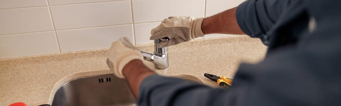 Male plumber repair sink faucet at customer kitchen. Maintenance and household assistance concept