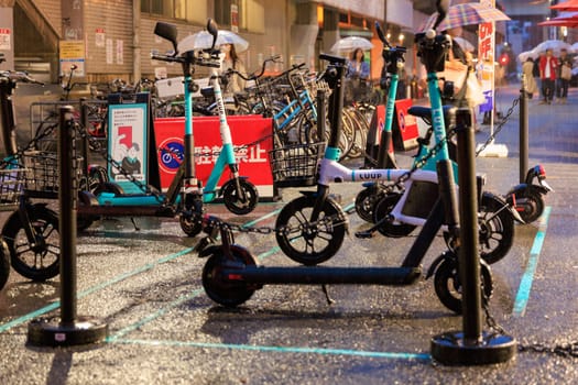 Osaka, Japan - April 29, 2023: Heavy rain on shared electric mini bikes and scooters parked on city street. High quality photo