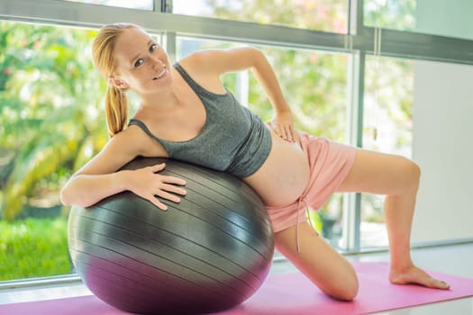 Pregnant woman exercising on fitball at home. Pregnant woman doing relax exercises with a fitness pilates ball. Against the background of the window.