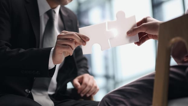 A business man sits at a table and holds a puzzle piece as a symbol of a business decision and success. business concept