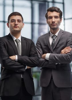 Two serious young businessmen standing with arms crossed in office