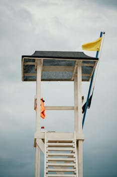 Empty white lifeguard tower with a yellow flag on the beach in windy weather. Beach lifeguard tower with yellow flag indicator. Nobody. Holiday recreation concept