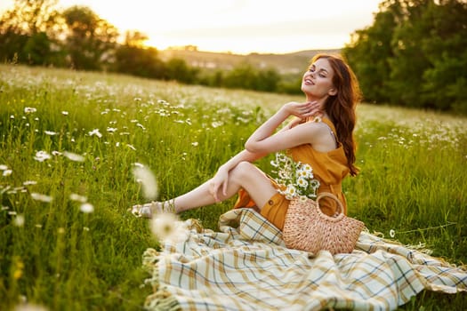 beautiful woman, in a summer orange dress enjoys nature while sitting in a chamomile field. High quality photo