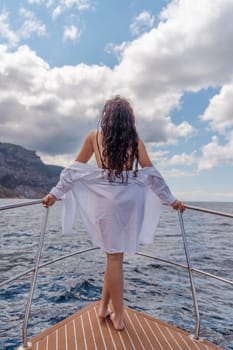 Woman on a yacht. Happy model in a swimsuit posing on a yacht against a blue sky with clouds and mountains.