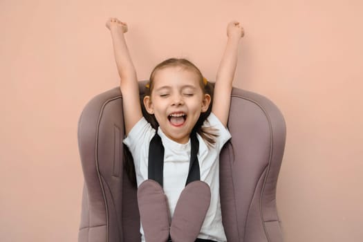 Funny happy caucasian girl of primary school age travels strapped in a car seat, studio portrait.