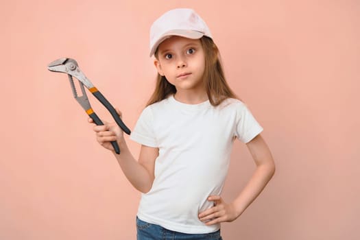 Caucasian girl of primary school age in a baseball cap with a wrench on a pink background.