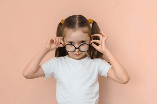 Portrait of a funny kid girl of elementary school age in round optical glasses on a pink background.