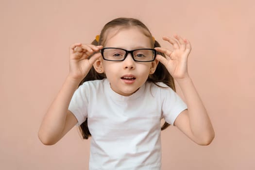 Cute Caucasian preschool girl with poor eyesight squints in rectangular glasses with ill-matched diopter.