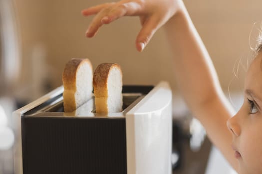 Close-up of a 5-7 year old girl who is preparing breakfast from toast in a toaster.