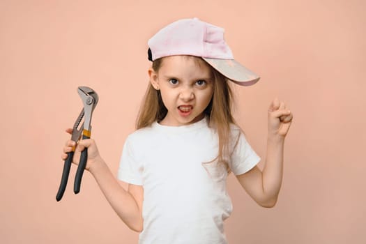 Cute little girl of primary school age in a baseball cap with a wrench on a pink background, dad's upbringing.