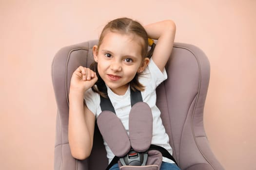 Funny smiling Caucasian preschool girl sitting in car seat looking at camera.