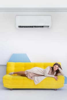 Young happy caucasian woman lies on a yellow sofa in bright interior with copy space, vertical.