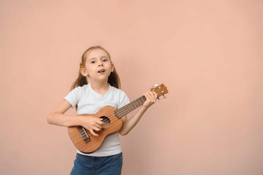 Kid girl in a white T-shirt with a ukulele on a pink background, copy space.