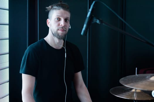 Portrait of a caucasian bearded drummer on a black stage behind a drum kit.