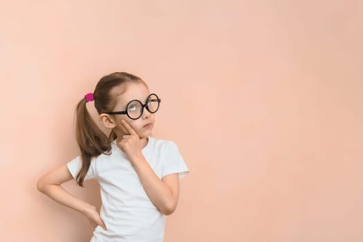 Thoughtful smart girl of elementary school age in round glasses against the pink background with copy space.