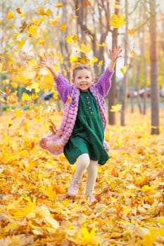 Joyful laughing caucasian girl 5 y.o. having fun in autumn park throws up fallen leaves.