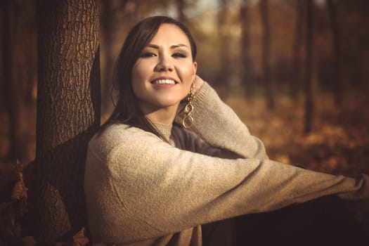 Young happy mixed race woman sitting on the grass in the park in autumn, toned photo.