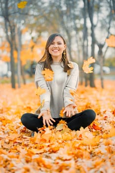 Happy mixed race fall young woman smiling joyful covered with autumn leaves outside in fall park, copy space.