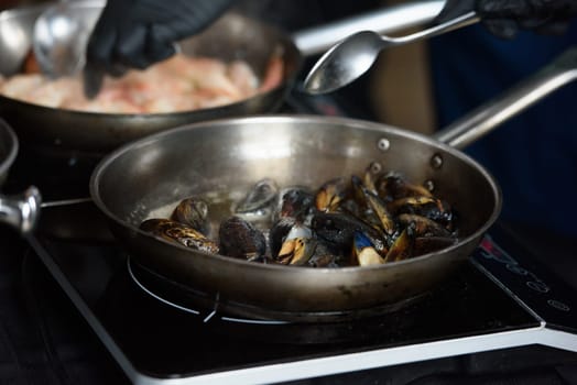 the chef in the restaurant is frying mussels in a steel pan.