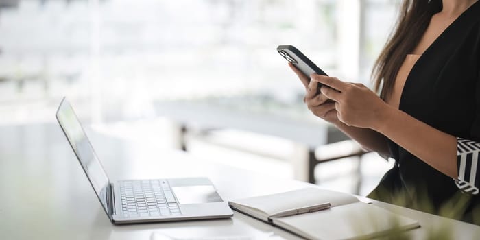 Asian businesswoman in formal suit in office happy and cheerful during using smartphone and working..