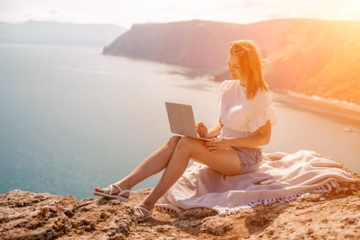 Freelance woman working on a laptop by the sea, typing away on the keyboard while enjoying the beautiful view, highlighting the idea of remote work