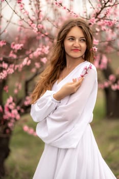 Woman peach blossom. Happy curly woman in white dress walking in the garden of blossoming peach trees in spring.