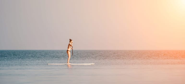 Silhouette of woman standing, surfing on SUP board, confident paddling through water surface. Idyllic sunset or sunrise. Sports active lifestyle at sea or river.