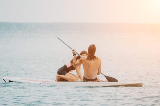 Sea woman and man on sup. Silhouette of happy young woman and man, surfing on SUP board, confident paddling through water surface. Idyllic sunset. Active lifestyle at sea or river