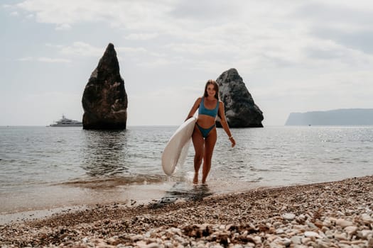 Close up shot of beautiful young caucasian woman with black hair and freckles looking at camera and smiling. Cute woman portrait in a pink bikini posing on a volcanic rock high above the sea