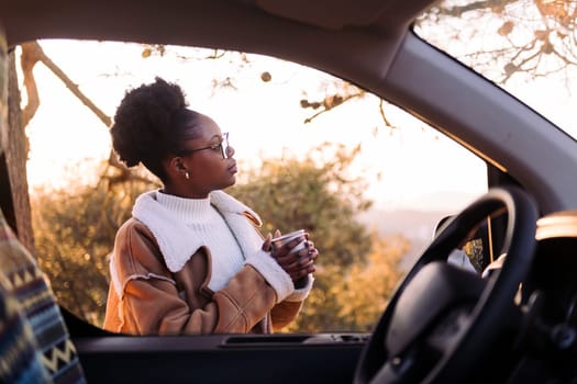 young african woman traveling in a camper van embraces the outdoors finding peace with tea in the morning, concept of nature's warmth and wilderness lifestyle