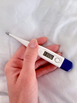 An electronic thermometer with a temperature of 37.5 in a female hand on a white blanket background. High quality photo