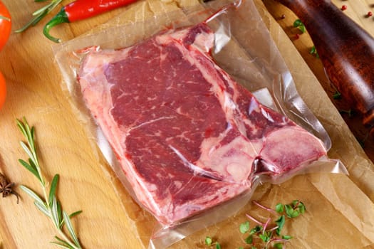 Raw meat in vacuum packaging on a wooden board with spices. Top view