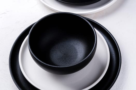 Different black and white empty plates and bowls on a white table.