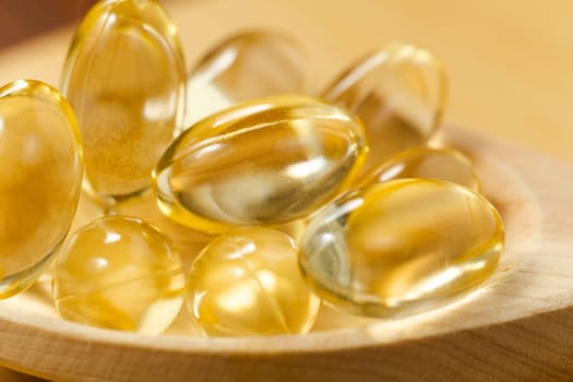 Yellow oil soft gel capsules in wooden background. Cosmetic pill capsule of vitamin E, A, almond oil, Omega 3, fish.