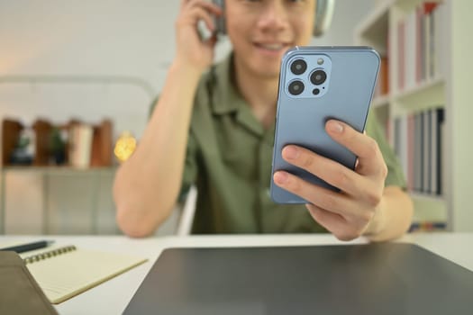 Selective focus on hand. Man holding smartphone over working desk, texting messages, chatting in social.