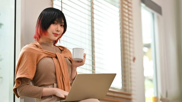 Young stylish woman using laptop at modern home office. Freelance, creative occupation, e-learning concept.